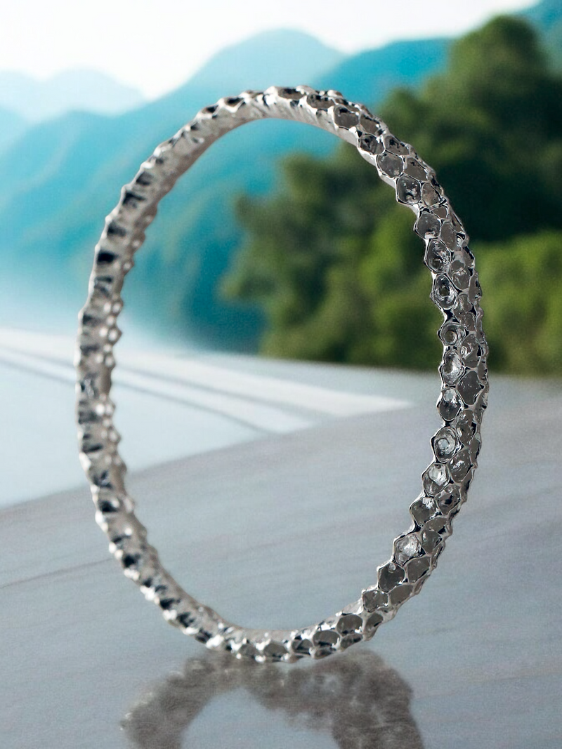 A Sterling Silver bracelet with a handmade design, displayed outdoors against a scenic mountain background